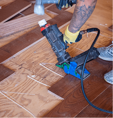 Professional installer using a flooring nailer to install hardwood planks